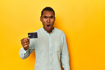 African American man with credit card, yellow studio, screaming very angry and aggressive.
