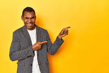 African American man in casual blazer, yellow studio, pointing with forefingers to a copy space,...