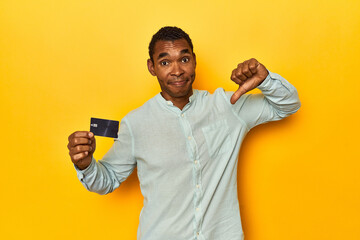 African American man with credit card, yellow studio, showing a dislike gesture, thumbs down....