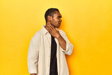 African American man with shirt, yellow studio, suffers pain in throat due a virus or infection.