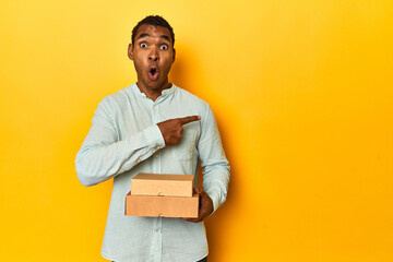African American man with food boxes, yellow studio, pointing to the side