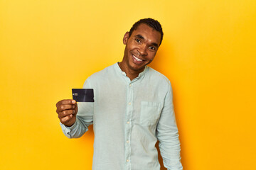 African American man with credit card, yellow studio, happy, smiling and cheerful.