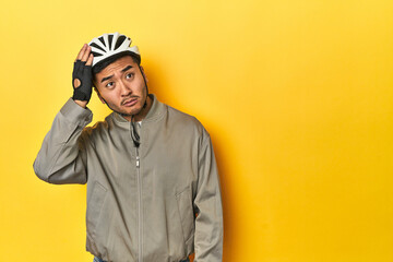 Asian man in bike helmet and gloves, yellow studio backdrop being shocked, she has remembered...