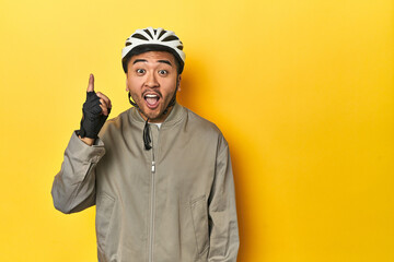 Asian man in bike helmet and gloves, yellow studio backdrop having an idea, inspiration concept.