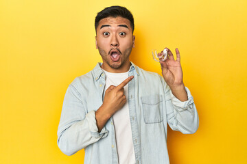 Asian man with invisible dental corrector, yellow studio backdrop pointing to the side
