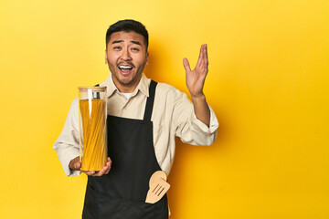 Asian chef with spaghetti jar, yellow studio backdrop receiving a pleasant surprise, excited and...