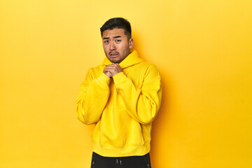 Bold Asian man in yellow hoodie on yellow studio scared and afraid.