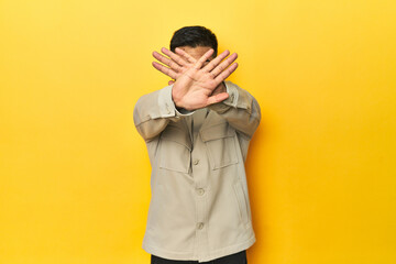 Asian man in stylish gray shirt on yellow studio doing a denial gesture