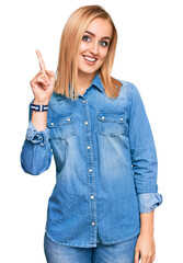 Beautiful caucasian woman wearing casual denim jacket showing and pointing up with finger number one while smiling confident and happy.