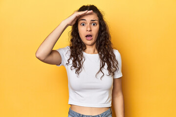 Young Caucasian woman, yellow studio background, shouts loud, keeps eyes opened and hands tense.