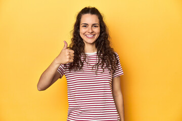 Young Caucasian woman, yellow studio background, smiling and raising thumb up