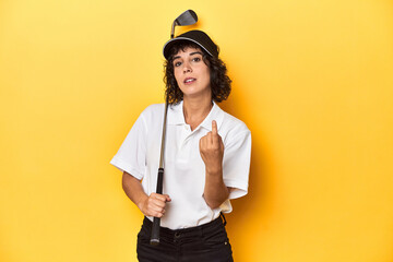 Athletic Caucasian woman with curly hair golfing in studio pointing with finger at you as if inviting come closer.