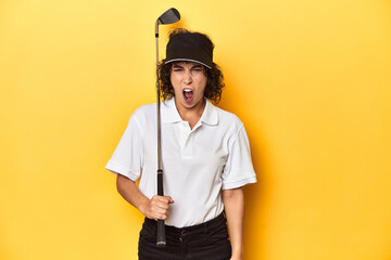 Athletic Caucasian woman with curly hair golfing in studio screaming very angry and aggressive.