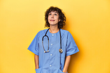 Curly-haired Caucasian woman nurse on yellow studio dreaming of achieving goals and purposes