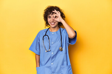 Curly-haired Caucasian woman nurse on yellow studio excited keeping ok gesture on eye.