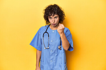 Curly-haired Caucasian woman nurse on yellow studio showing fist to camera, aggressive facial...