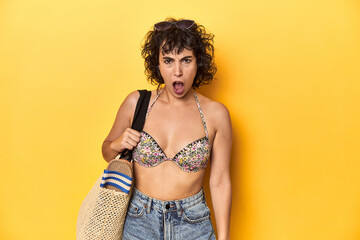 Caucasian woman in bikini with beach bag, studio screaming very angry and aggressive.