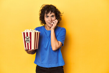 Curly-haired woman with popcorn for movie, studio biting fingernails, nervous and very anxious.