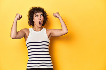 Caucasian curly-haired woman in white tank-top raising fist after a victory, winner concept.