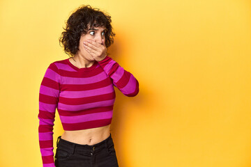 Caucasian curly-haired woman in pink striped-top thoughtful looking to a copy space covering mouth...