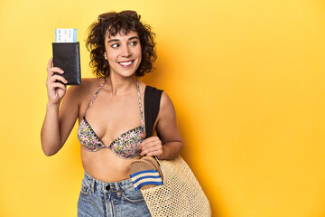Curly-haired woman with beach gear and volleyball, yellow studio backdrop.