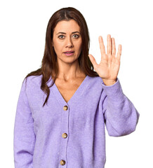 Elegant middle-aged Caucasian woman in studio setting standing with outstretched hand showing stop sign, preventing you.