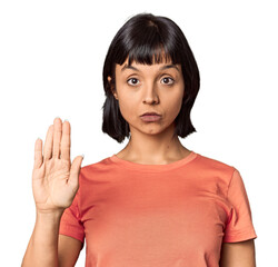 Young Hispanic woman with short black hair in studio standing with outstretched hand showing stop sign, preventing you.