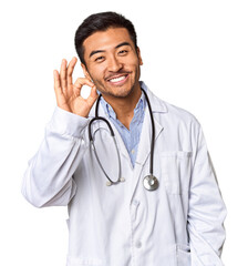 Young Chinese man as a medical doctor in studio cheerful and confident showing ok gesture.