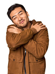 Young Chinese man in studio background hugs, smiling carefree and happy.