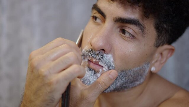 Handsome guy shaving with a razor at home