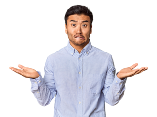 Young Chinese man in studio background confused and doubtful shrugging shoulders to hold a copy space.