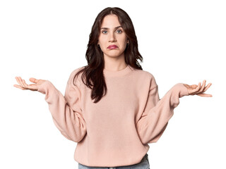 Young Caucasian woman in a studio setting doubting and shrugging shoulders in questioning gesture.