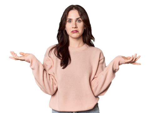 Young Caucasian woman in a studio setting doubting and shrugging shoulders in questioning gesture.