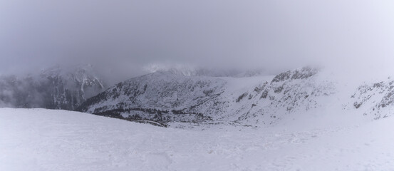 Obraz premium The white snow peaks of Pirin partly covered by fog. Snowy weather conditions for winter sports and tourism. Alpine ski resort Bansko, Bulgaria.