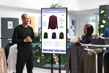 Male customer is shown clothing on an interactive kiosk board by female assistant in mall clothing...