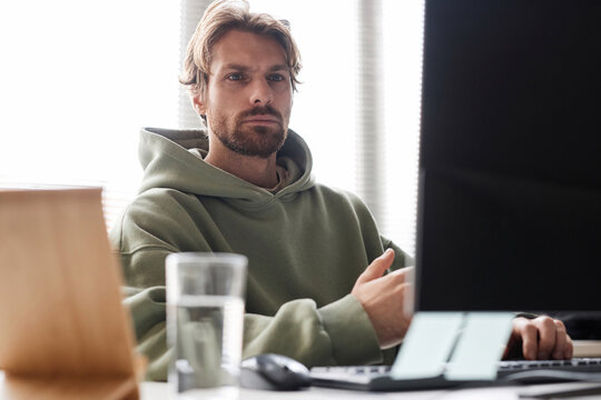 Front view portrait of bearded software programmer looking at computer screen with focused face expression while working in office