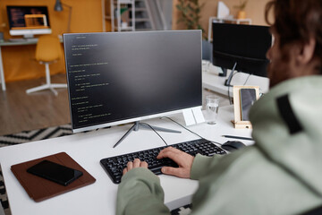 Over shoulder view at software developer writing code in office with focus on computer screen, copy space