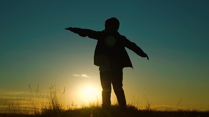 Child boy play like an airplane, in park opposite sky at sunset. Boy aviator dreaming raised his...