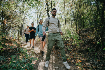Naklejka na ściany i meble A group of friends hiking through a green forest, enjoying a sunny day in the wilderness. They embrace a healthy lifestyle, discussing different topics and having fun.