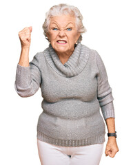 Senior grey-haired woman wearing casual winter sweater angry and mad raising fist frustrated and...