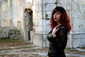 Fototapeta na wymiar Amidst ruins, a red-haired dark beauty, half-bust framed, explores the mystery of an abandoned abbey with a haunting allure.