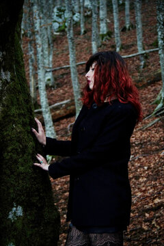 Mysterious woman amid trees, silhouette contrasting with filtered light, dark attire harmonizing with nature, creating an ethereal atmosphere.