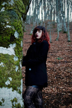 Mysterious woman amid trees, silhouette contrasting with filtered light, dark attire harmonizing with nature, creating an ethereal atmosphere.