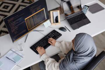 Top view at Muslim young woman writing code with multiple computer devices and wearing modest clothing