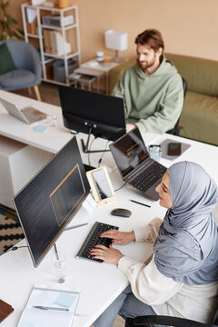 High angle portrait of two people working in IT developers office with Muslim young woman as female programmer writing code