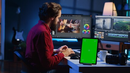 Video editor adds sound effects to filmed footage, working in post production studio with green screen tablet. Videographer using headphones to test and improve audio quality next to mockup device - obrazy, fototapety, plakaty