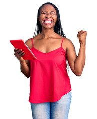 Young african american woman holding touchpad screaming proud, celebrating victory and success very excited with raised arms