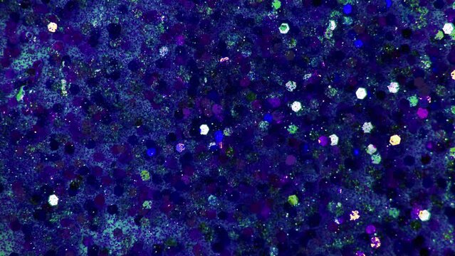 Multicolored blue particles like confetti or spangles float in a viscous liquid and glitter in the light with depth of field. Glitter texture. Particles blue background. Shining sparkles. 