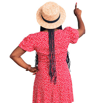 Young african american woman wearing summer hat posing backwards pointing ahead with finger hand