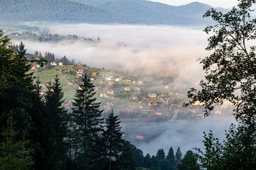 Aerial view over the village with a sea of fog or clouds, mountains on background during the early morning